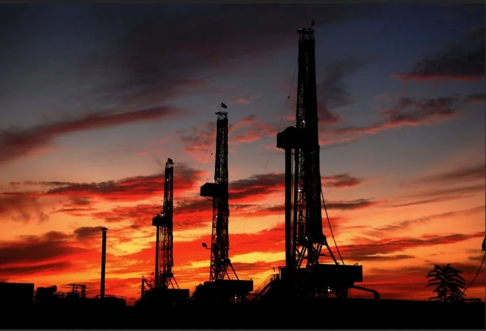 A group of drilling rigs in the sunset.